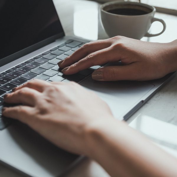 Closeup image of a woman working and typing on laptop keyboard with coffee cup on the table