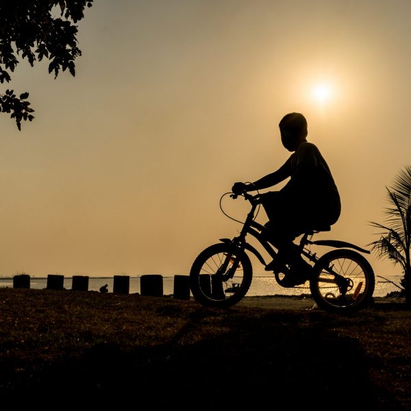 silhouette of the boy riding bike under the sunset near the beach on his holiday vacation relaxing time